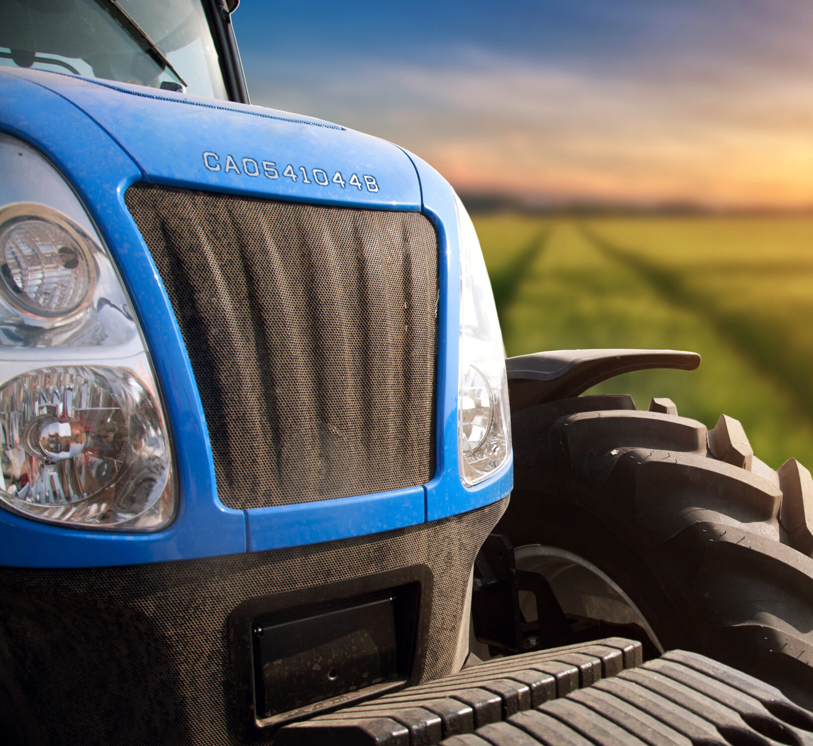 Modern tractor on a field with green wheat at sunset.